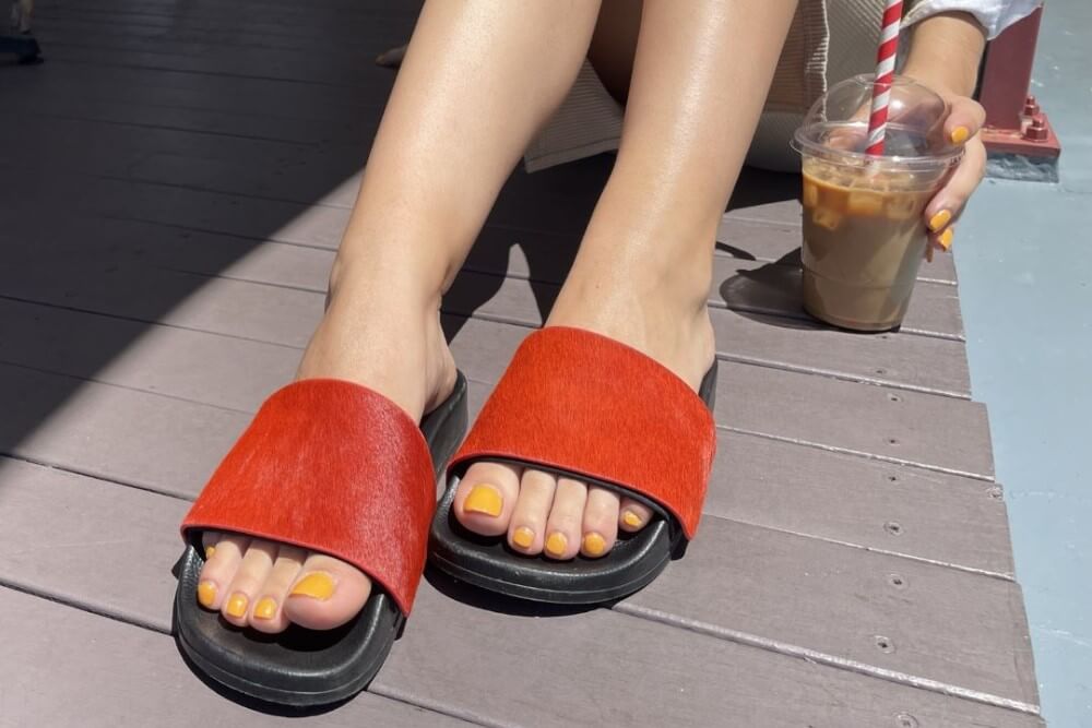 Woman having an iced coffee wearing black Chimissimi slides with red Rita uppers
