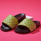 Australian designer black slides with upper in green quilted fabric over pink background.
