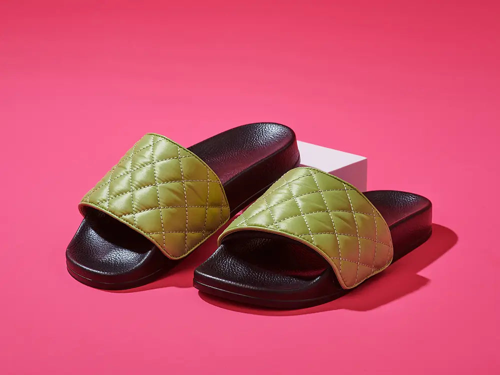 Australian designer black slides with upper in green quilted fabric over pink background.