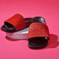 Black slides with red upper made of real cow fur over pink background.