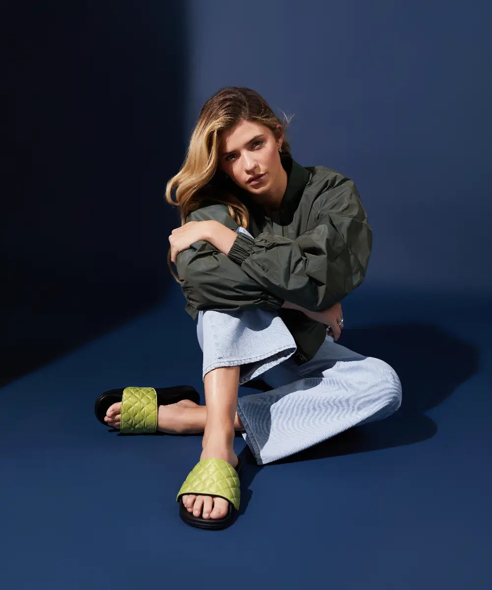 Model wearing casual outfit with jeans and black slides with upper in green quilted fabric.