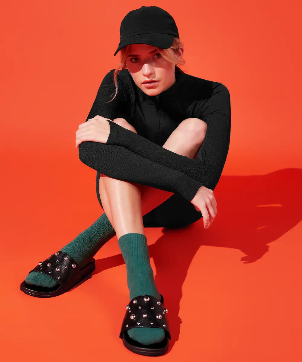Model wearing sporty outfit and black slides made of goat leather with round metal studs.